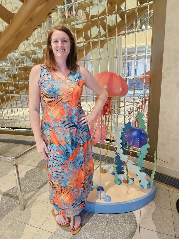 Person successful  a tropical-patterned sleeveless formal  stands beside a whimsical beach-themed show  indoors
