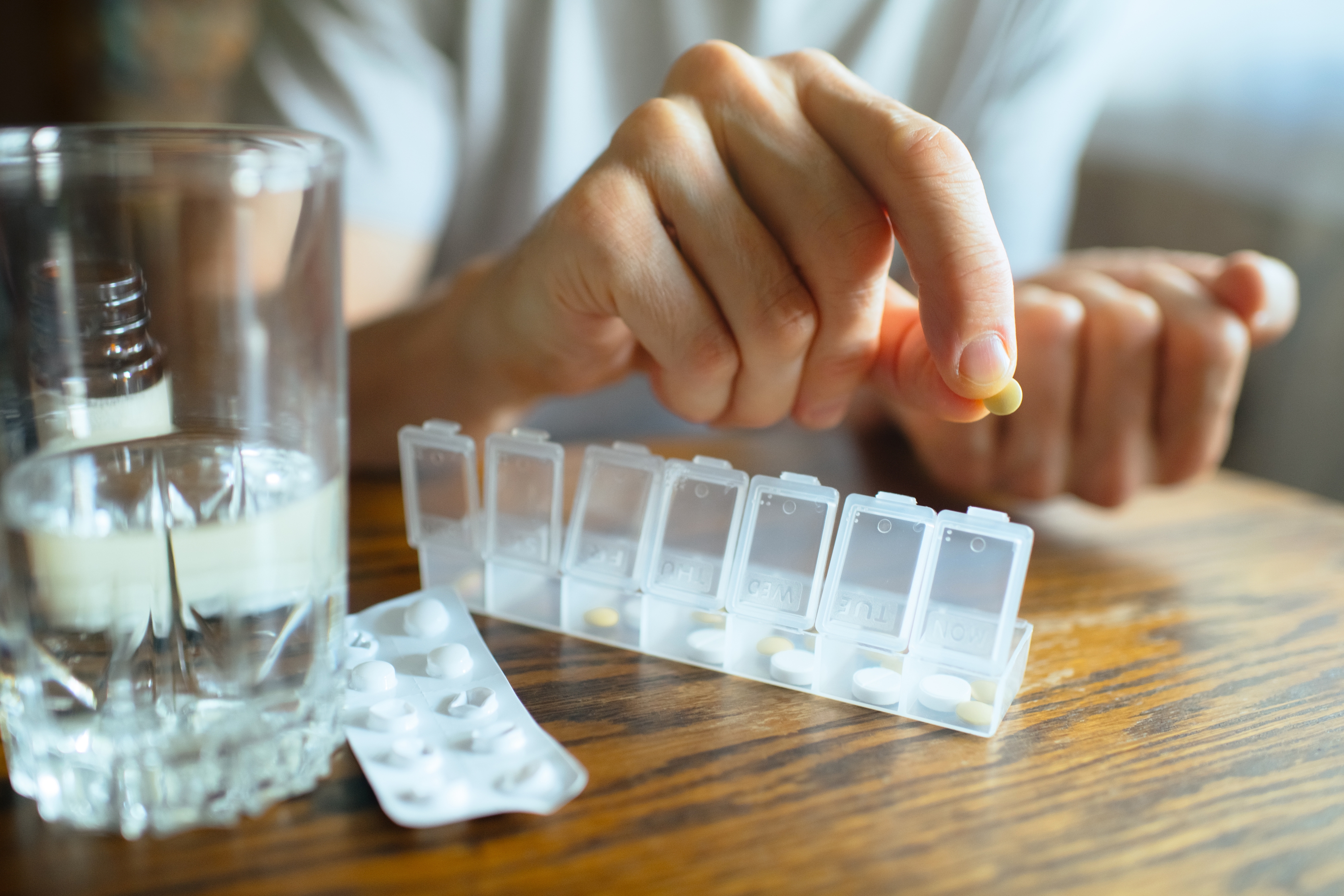 Person som organiserer piller i en ukentlig pillearrangør, med et glass vann og en pakke med tabletter i nærheten