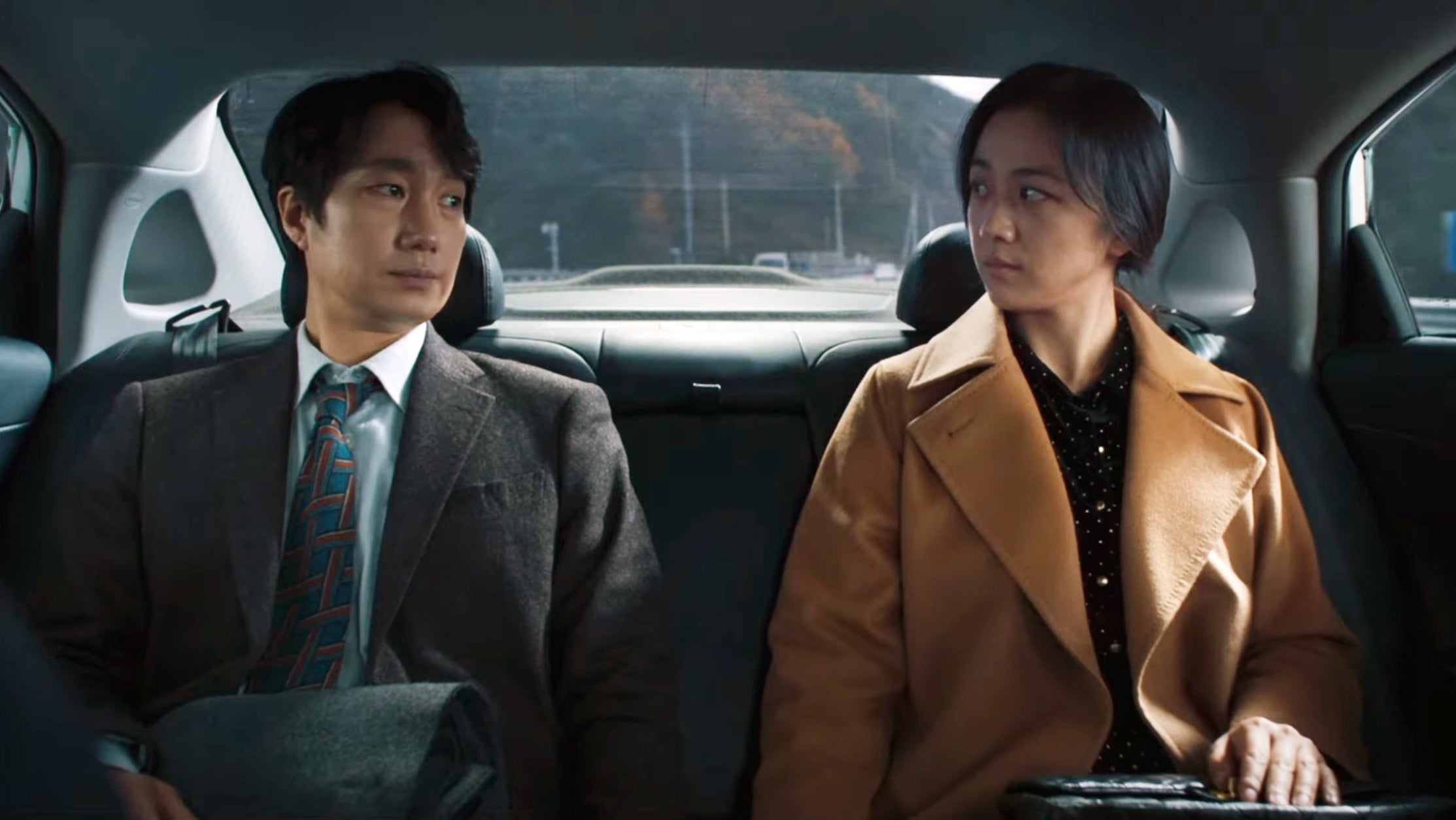 Two radical   beryllium   successful  the backmost  spot   of a car, engaged successful  a superior   conversation. One wears a suit, the different   wears a agelong  coat