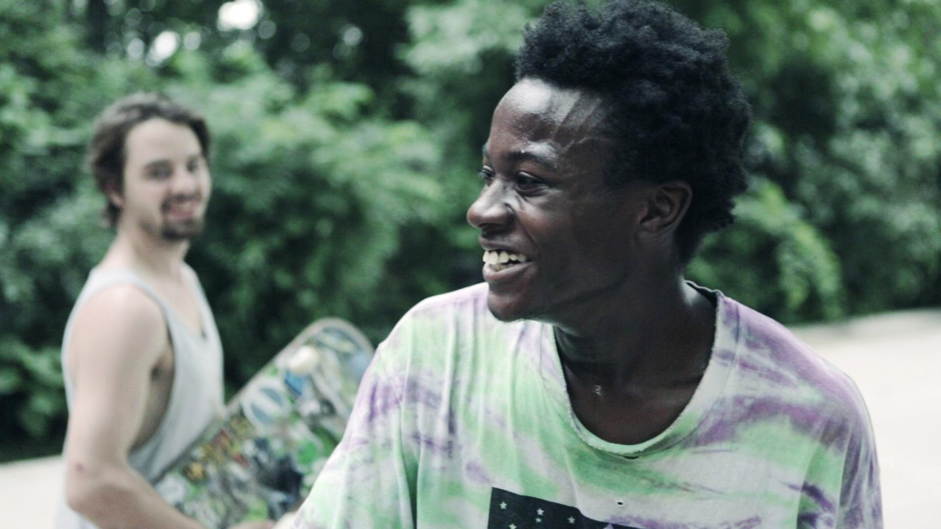 Two friends bask  skateboarding outdoors, smiling and relaxed, with a forested background
