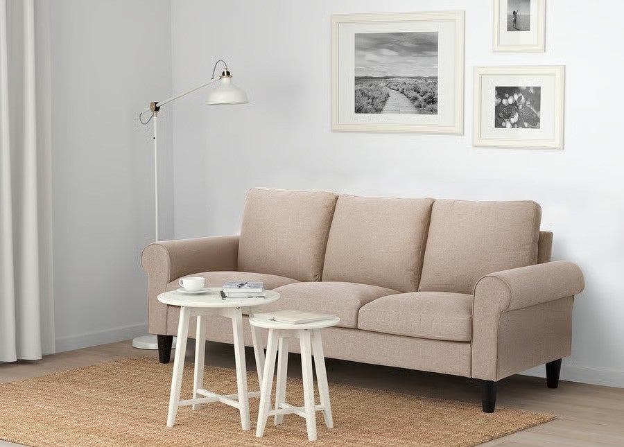 Neutral-toned living room with a three-seater sofa, nested coffee tables, and framed wall art, creating a cozy shopping catalog scene