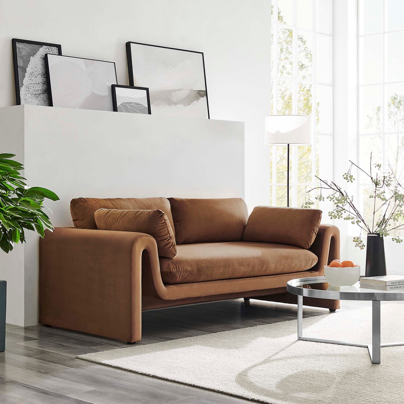 Modern living room with a stylish brown couch, abstract art on a ledge, a round coffee table, and potted plants for a cozy shopping feature