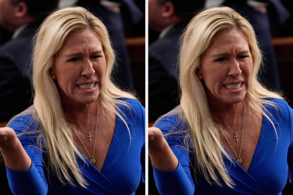 Person in formal setting gesturing expressively, wearing a blue dress with a cross necklace
