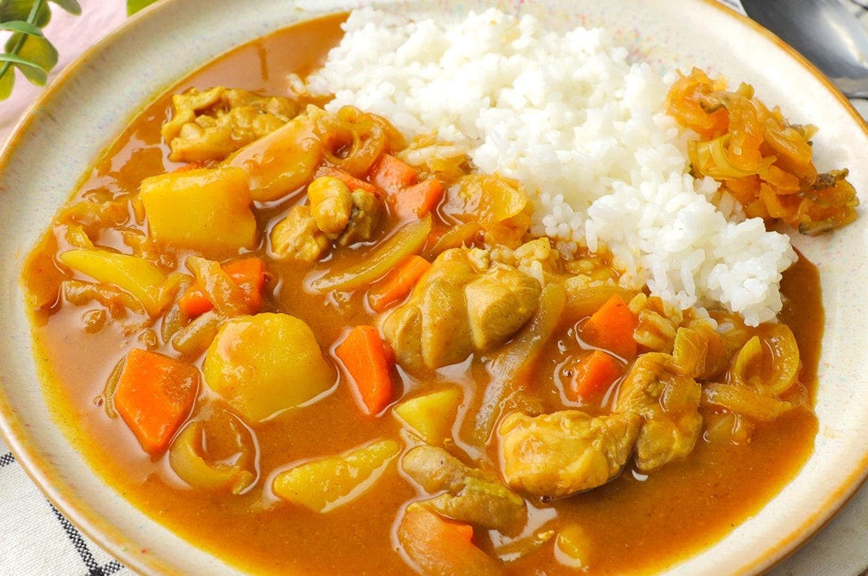 カレーライスの皿。鶏肉と野菜が含まれ、ライスと一緒に盛り付けられている。