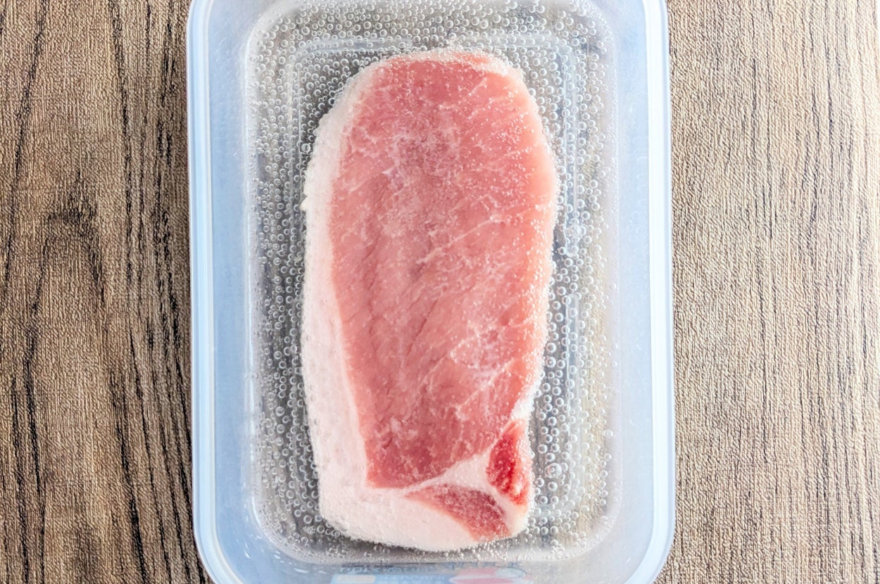 プラスチック容器に入った1枚の豚肉が木目のテーブルに置かれている。