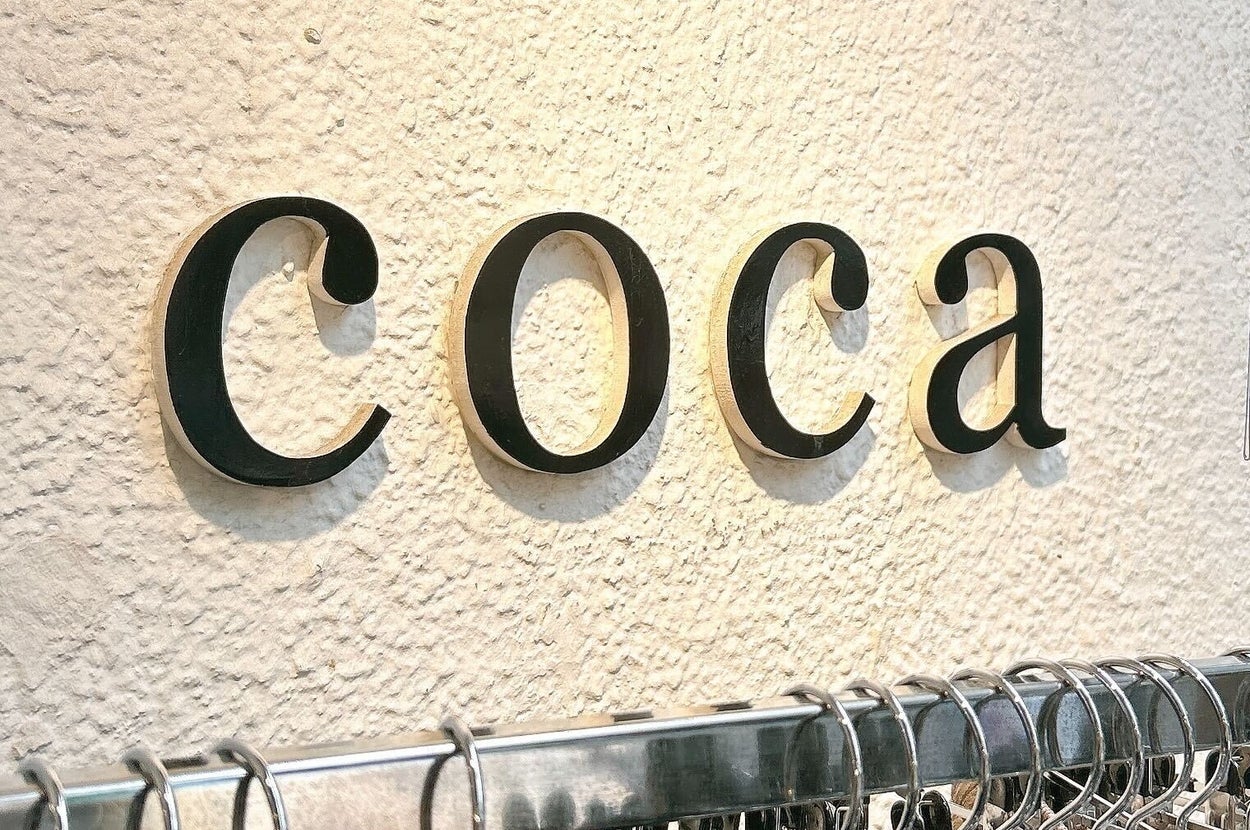 店の壁に「coca」の文字が表示され、下には服がハンガーにかかっている。