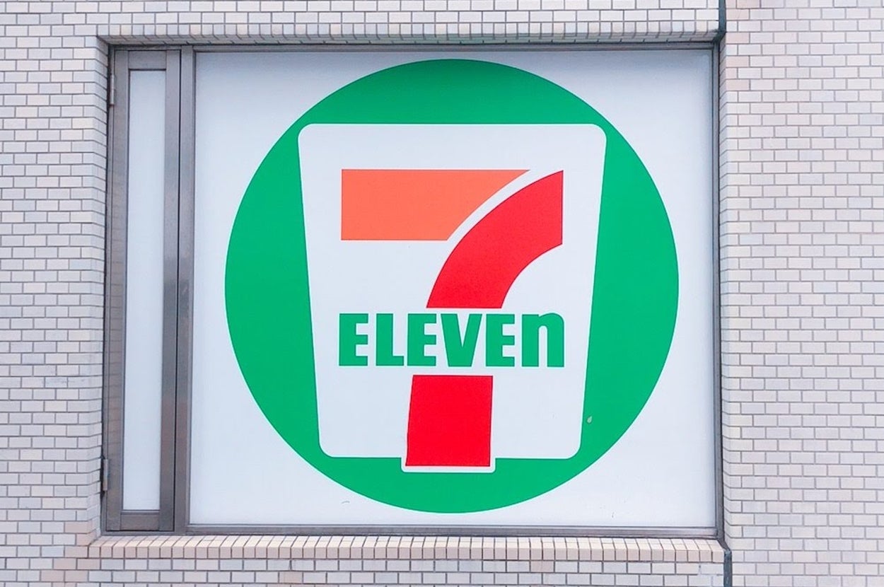 セブン-イレブンの入り口で、店舗ロゴとたばこ自販機が見える風景。