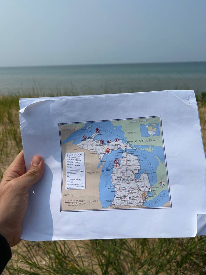 Person holds a printed representation of Michigan adjacent a lake. Locations are marked with reddish circles connected the map