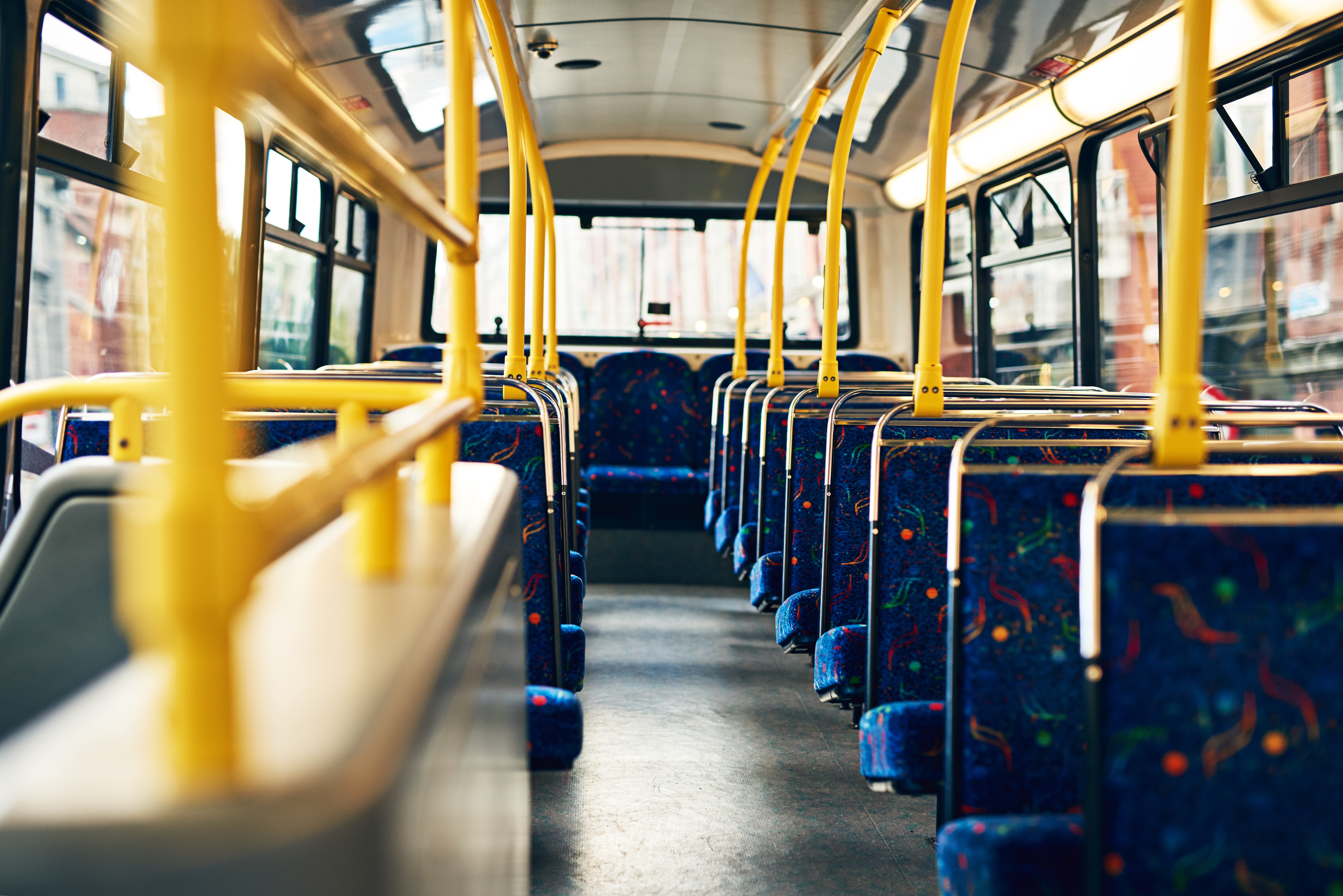 Interior of an empty double-decker bus with patterned seats and yellow handrails, viewed from the back