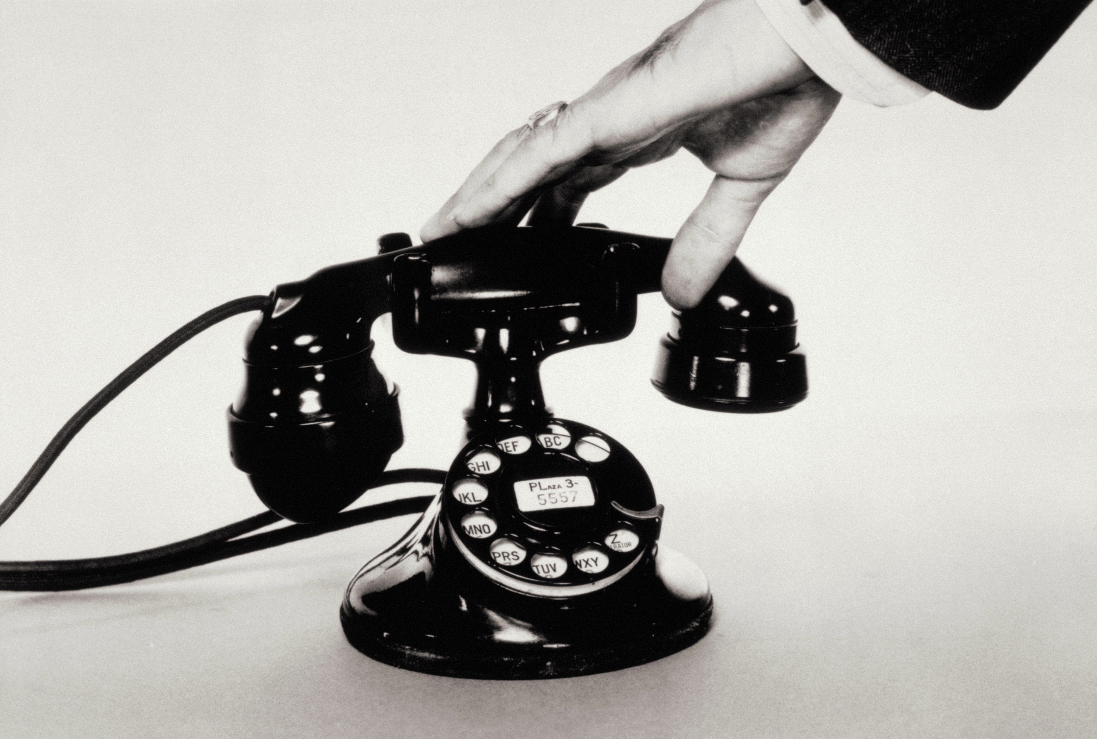 A hand reaches for the receiver of a vintage rotary dial telephone