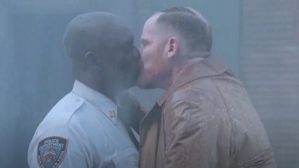 Captain Holt in his police uniform and Kevin in a trench coat kiss in the rain