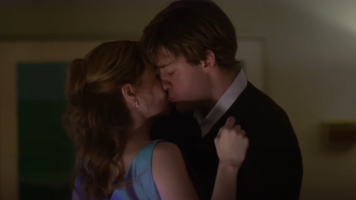 Pam and Jim in formal attire share a gentle kiss in dim light