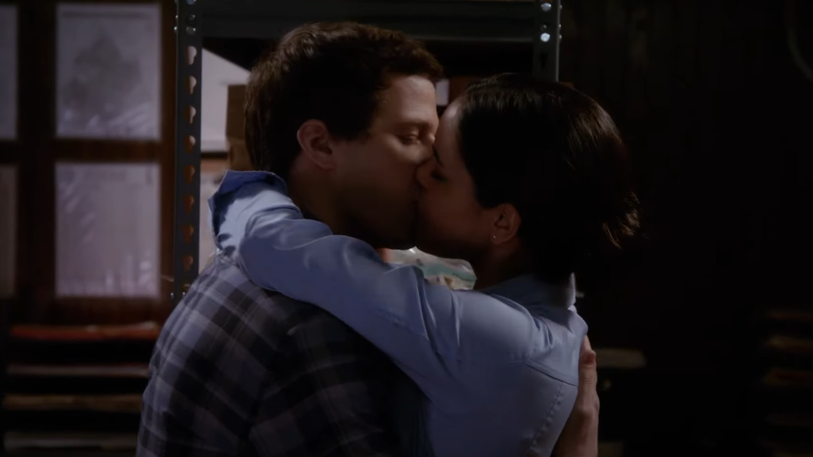 Jake and Amy kiss in dim light, arms wrapped around each other