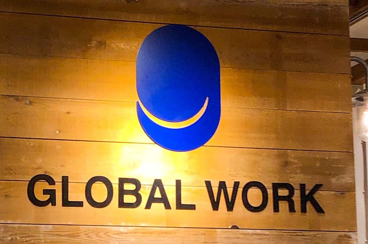 木製の壁に掲げられた「GLOBAL WORK」のロゴとその照明。