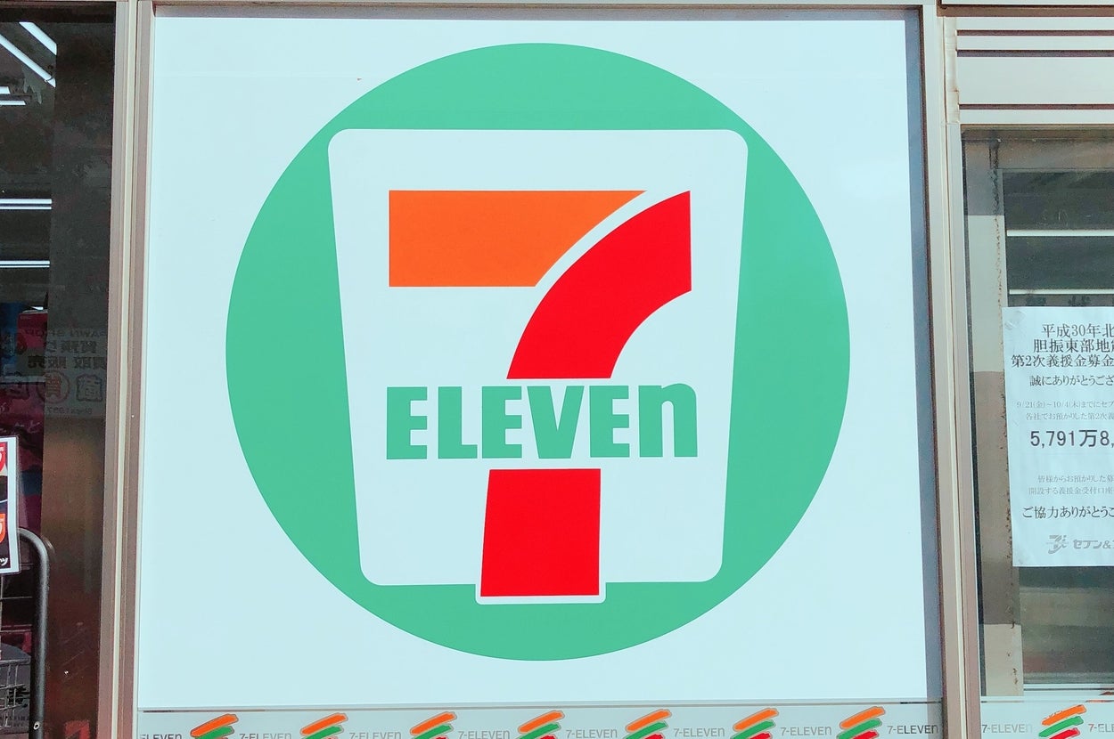 セブンイレブンの看板があり、店の外観が見えます。店舗の広告が横に貼られています。