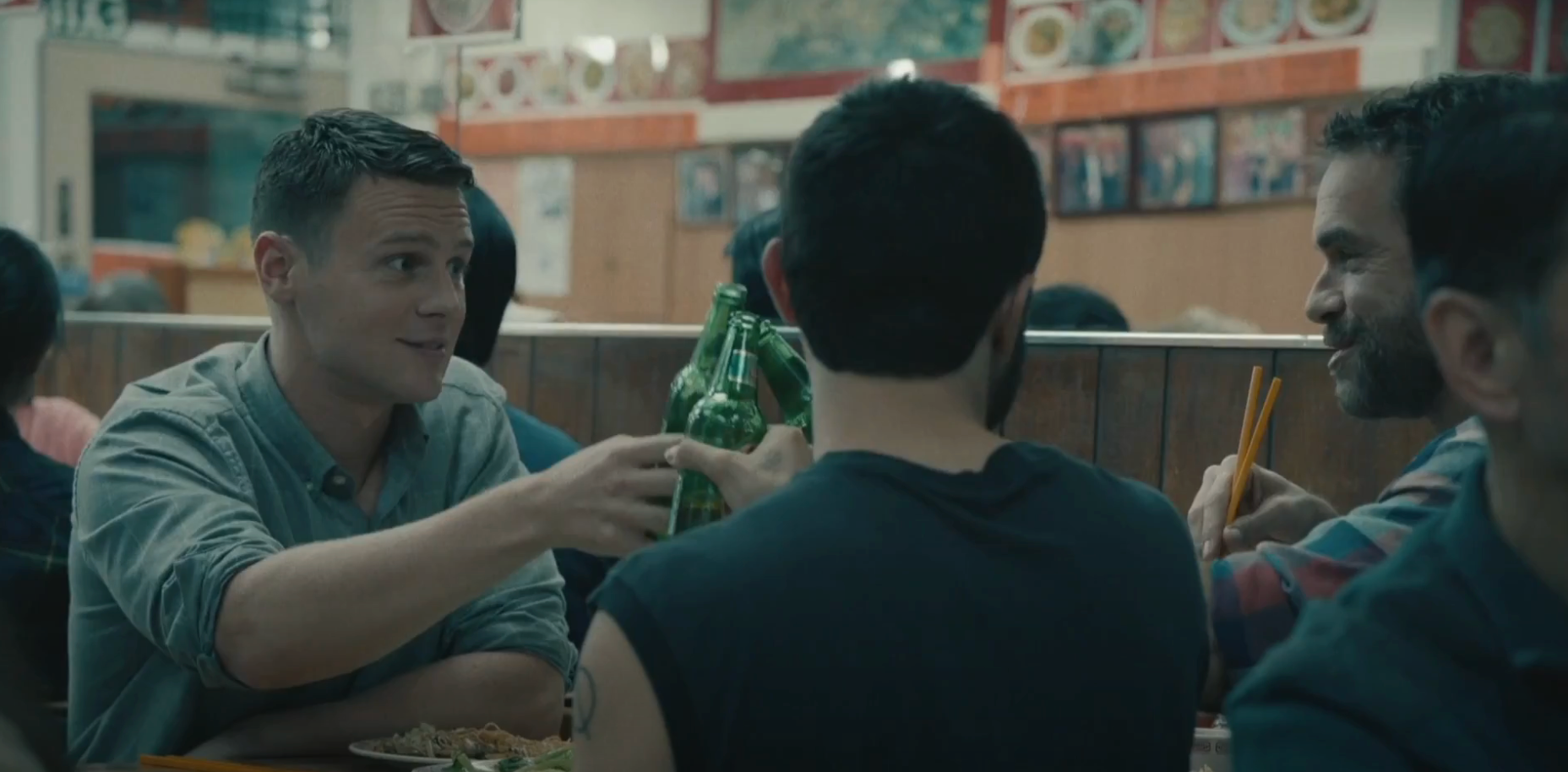 People enjoying a meal together in a busy restaurant, raising bottles in a toast, conveying a casual and friendly atmosphere