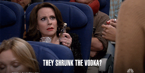 A surprised woman on an airplane holds a small vodka bottle, and the text reads, "They shrunk the vodka"