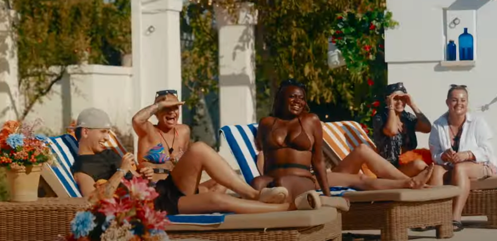 A group of people relax on sun loungers by a pool, smiling and enjoying each other's company