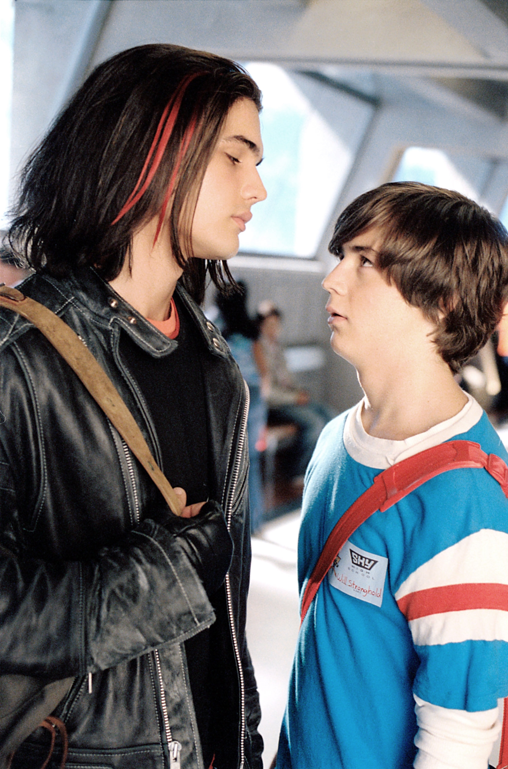 Two young men face each other in a tense scene; one wears a leather jacket, and the other a casual striped shirt
