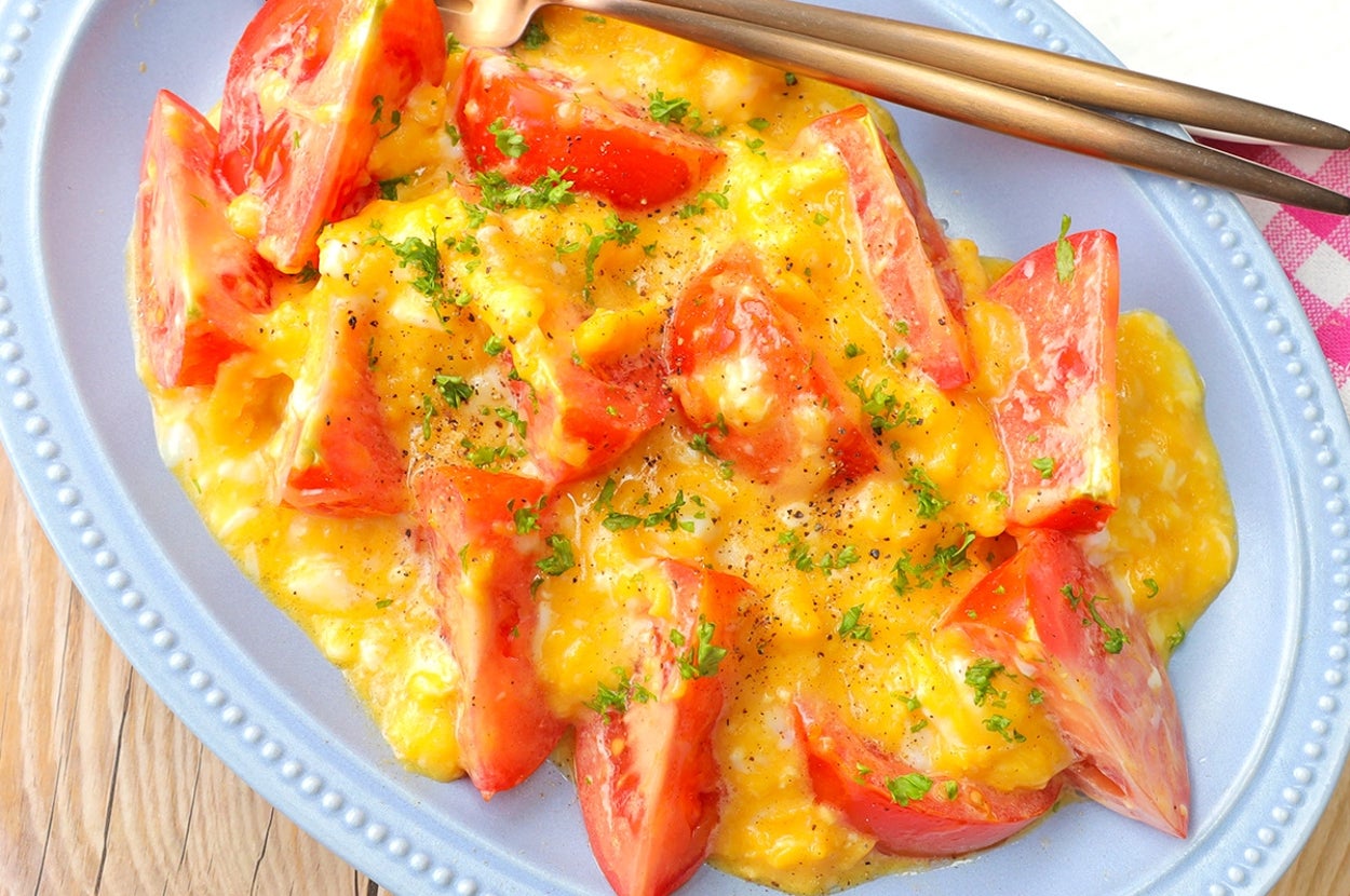 お皿に盛り付けられたトマトとスクランブルエッグ料理。トッピングにハーブが少々。フォークとスプーンが添えられている。