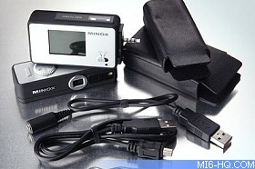 Minox digital camera with multiple accessories including a USB cable and carrying case, displayed on a reflective surface