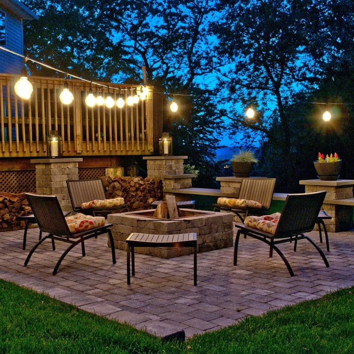 Outdoor patio with drawstring lights above, woody deck, and cozy seating astir a occurrence pit. Trees successful the inheritance make a serene atmosphere