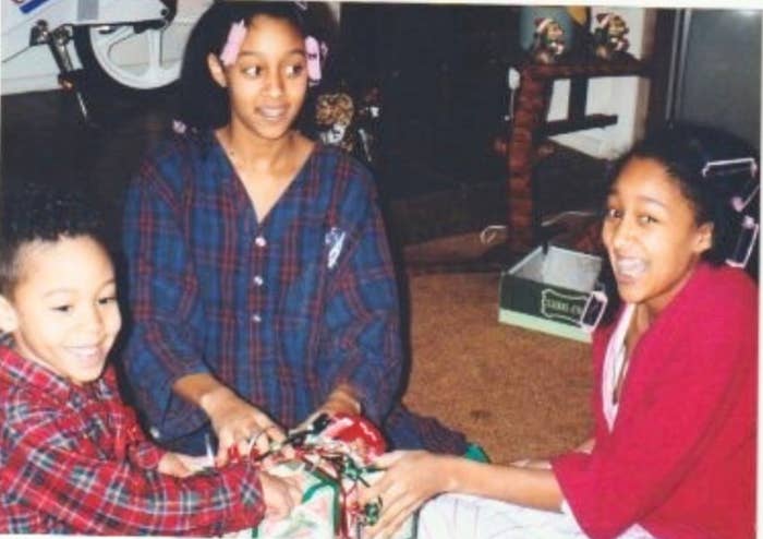 Three children in pajamas excitedly open a present together at home, with a bicycle visible in the background