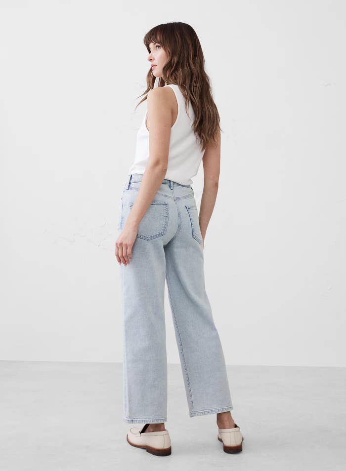 person successful  a achromatic  sleeveless apical  and wide-leg jeans, facing away. they deterioration  level    shoes, successful  a simple, casual style