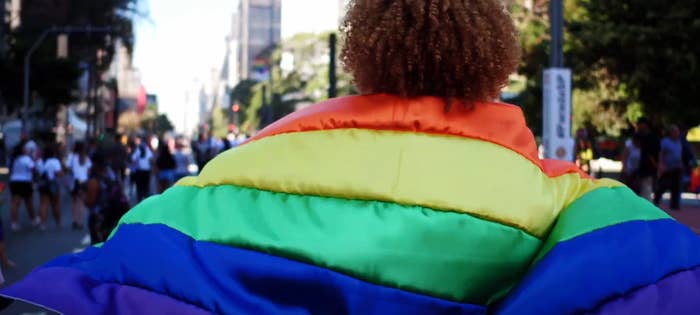 Person wearing a rainbow flag draped over their shoulders, standing on a bustling city street