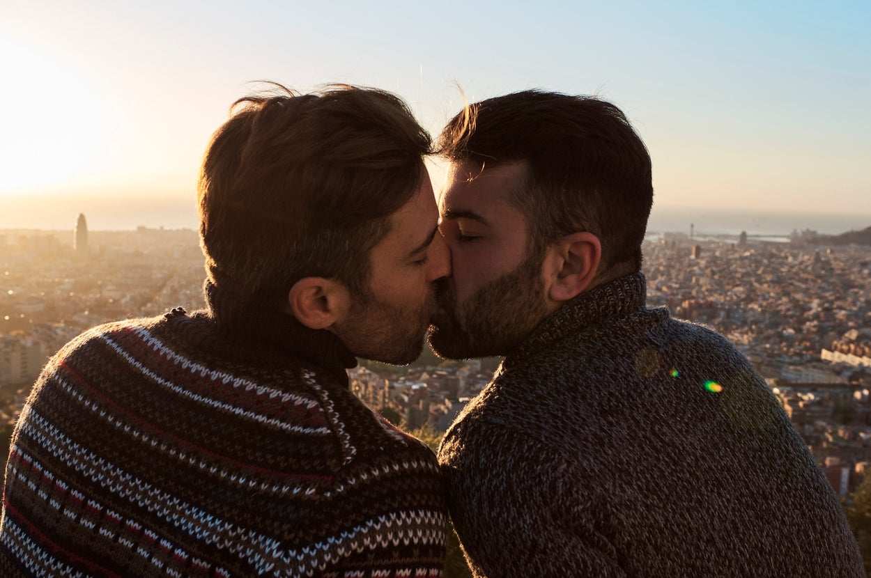 Two men kissing with a cityscape view at sunset in the background