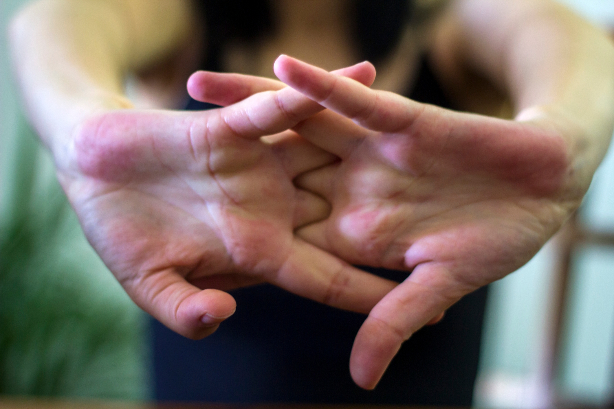 Hender som strekker seg fremover med fingrene sammenlåst, noe