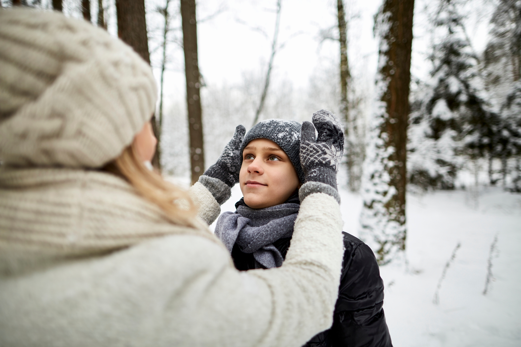 Person om vinteren tilpasser en annen hatt i en snødekt skog, og formidler varme og omsorg