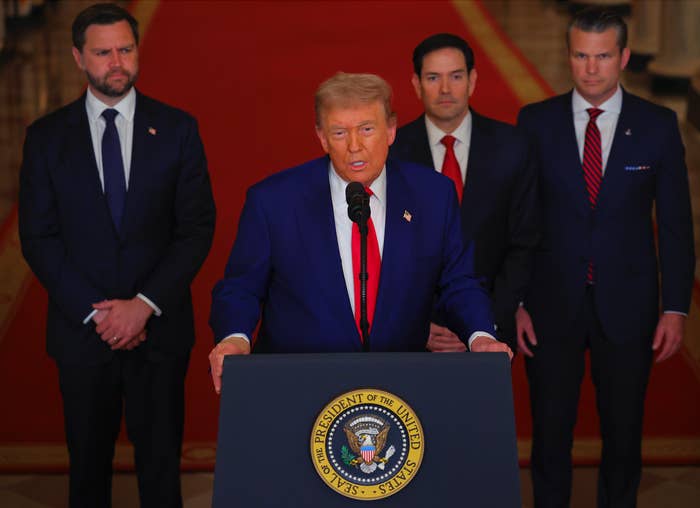 Donald Trump stands at a podium with the presidential seal, delivering a speech. Three individuals in suits stand behind them on a red carpet