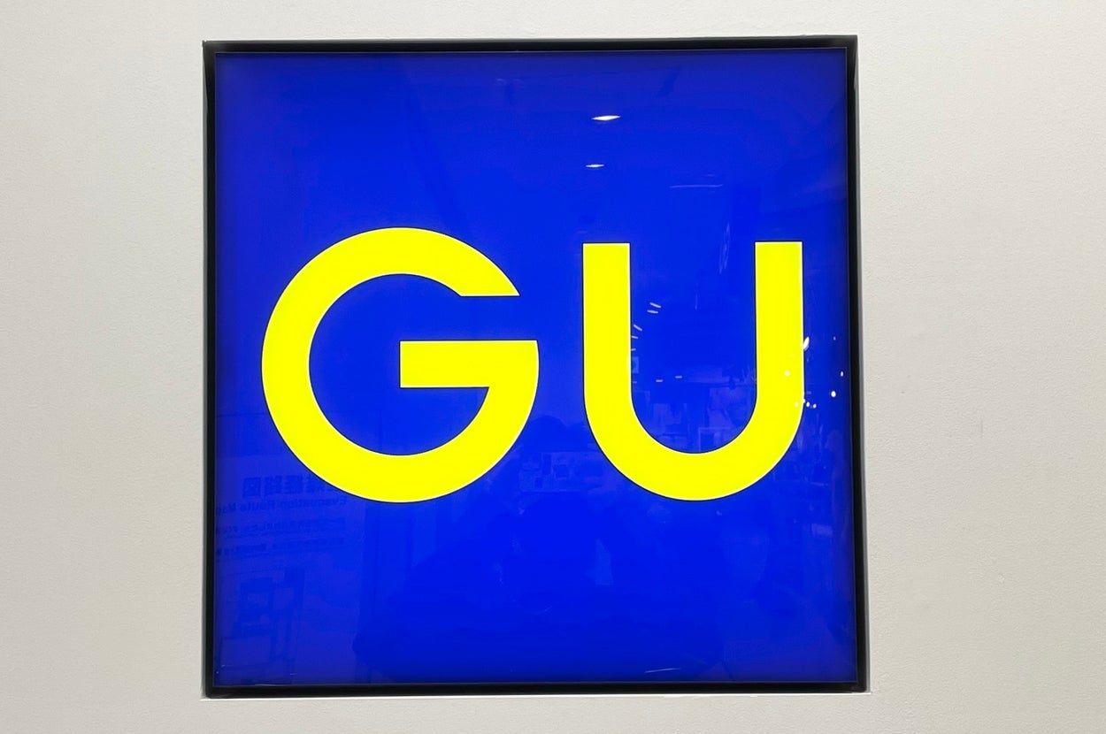A sign with large yellow letters "GU" on a blue background, mounted on a wall