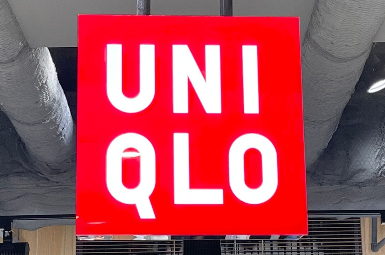 UNIQLO store sign mounted on ceiling, with shelves of folded clothing and price signs visible below