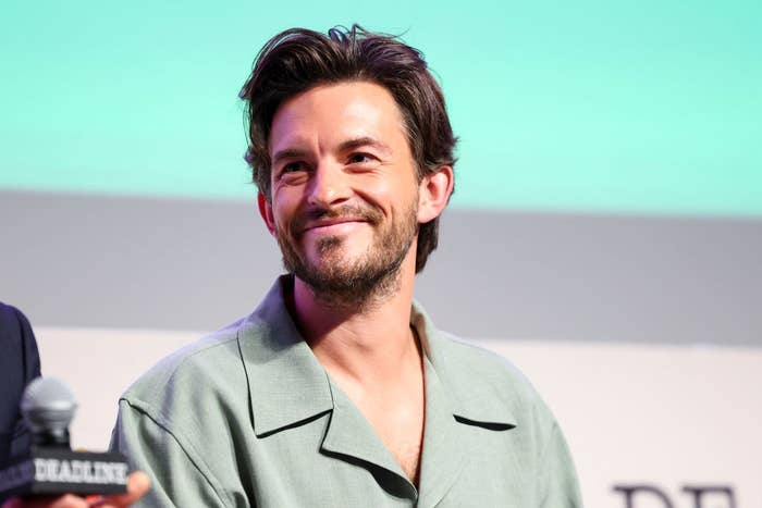 Man in casual shirt smiles while holding a microphone at an event panel