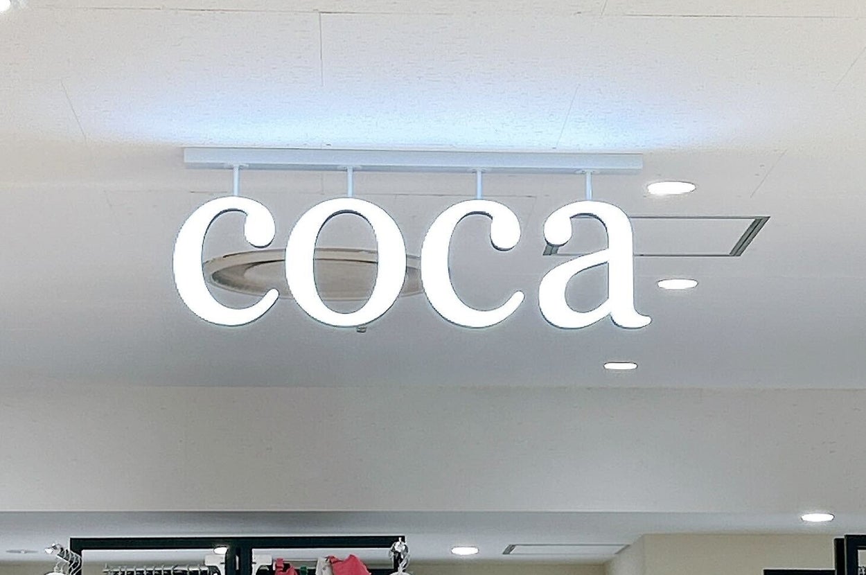 店内の上部に「coca」と書かれたネオンサインが設置されている。下には衣類が陳列されている。