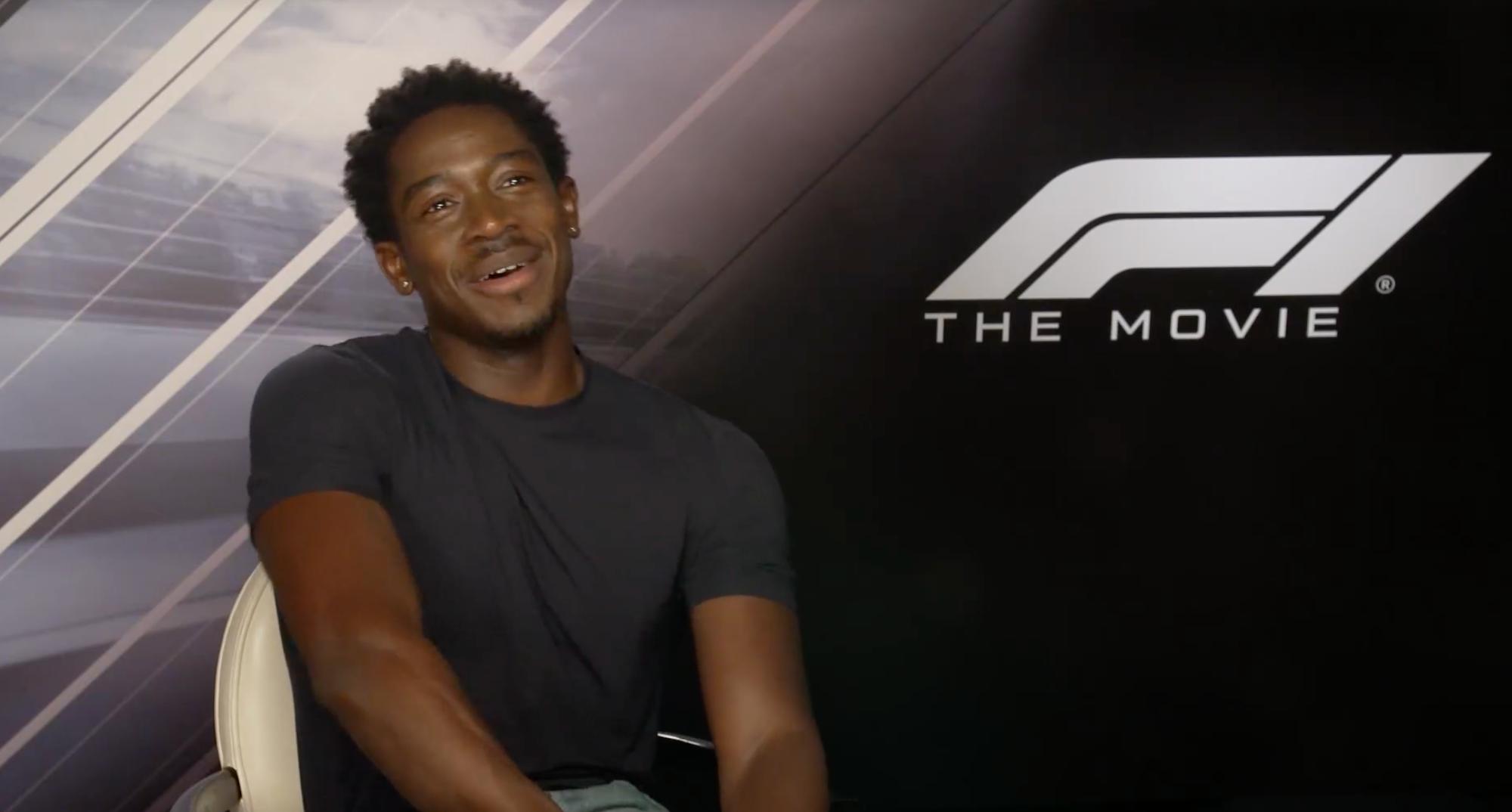 Person smiling while seated in front of "F1 The Movie" backdrop