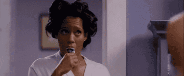 A person with hair in rollers brushes their teeth, wearing a robe, in a casual setting