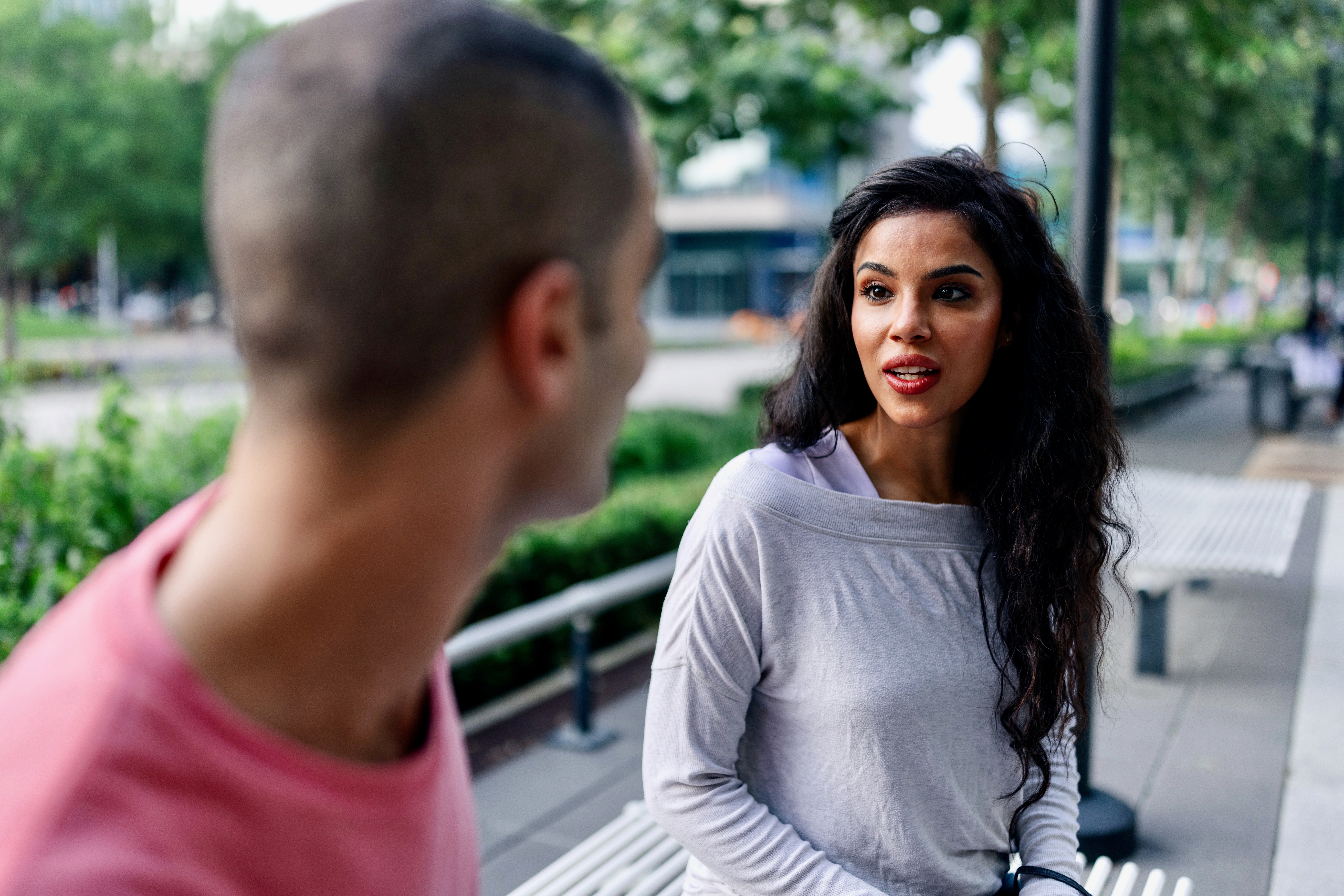 Two people sit on a bench outdoors, engaged in conversation