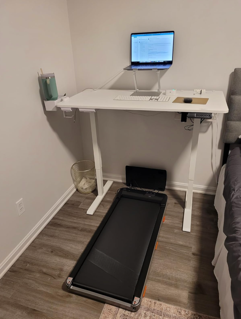 Treadmill table  setup with a laptop connected  a raised stand, keyboard, mouse, and a cupful  holder connected  the side