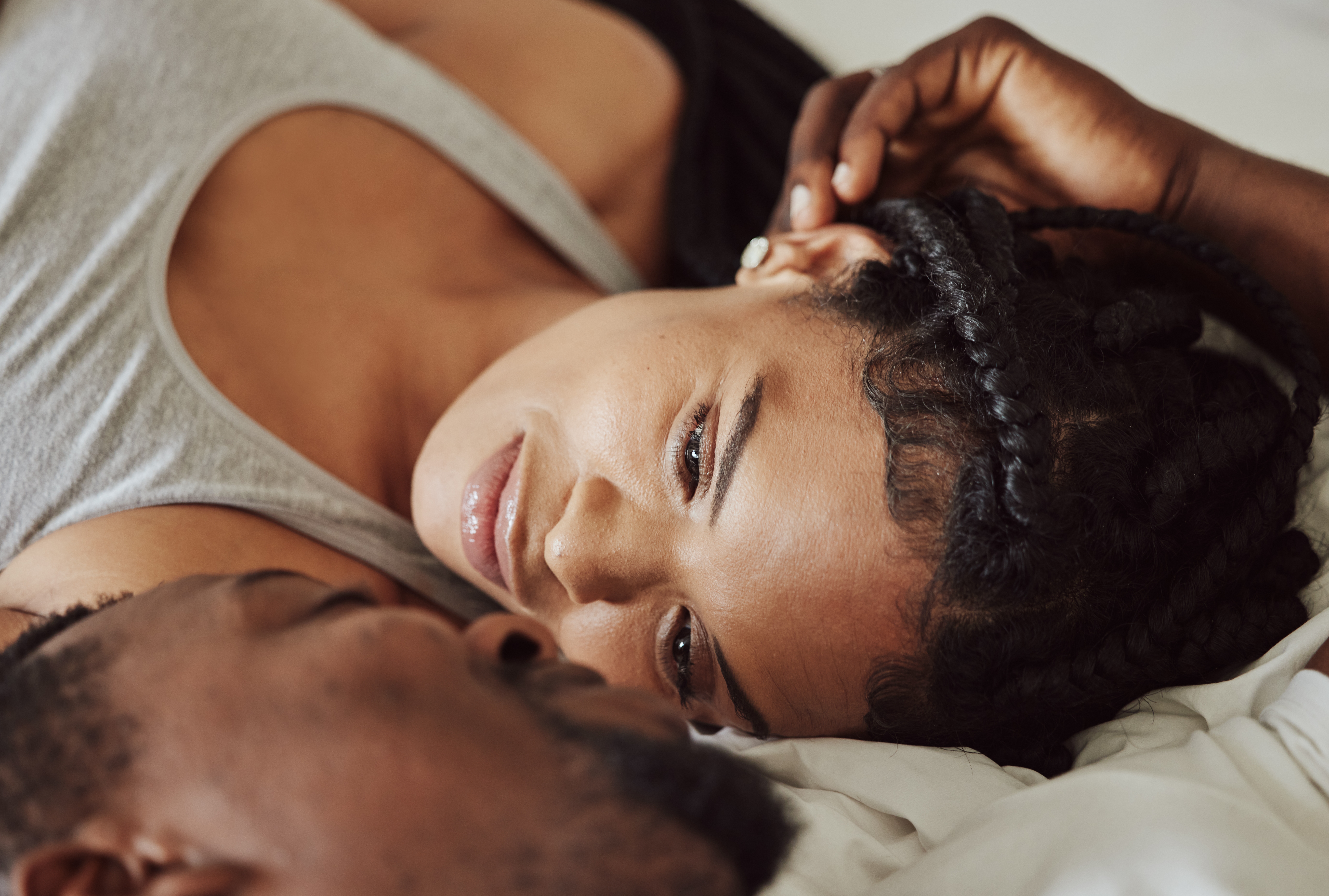 A woman with braided hair lies on a bed, gazing softly into the face of another person