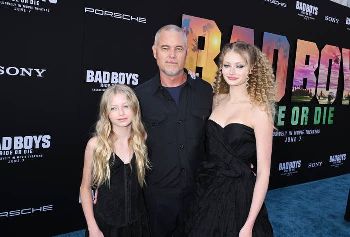 Two individuals in black attire on a red carpet with a man in a dark suit at a "Bad Boys" movie event backdrop