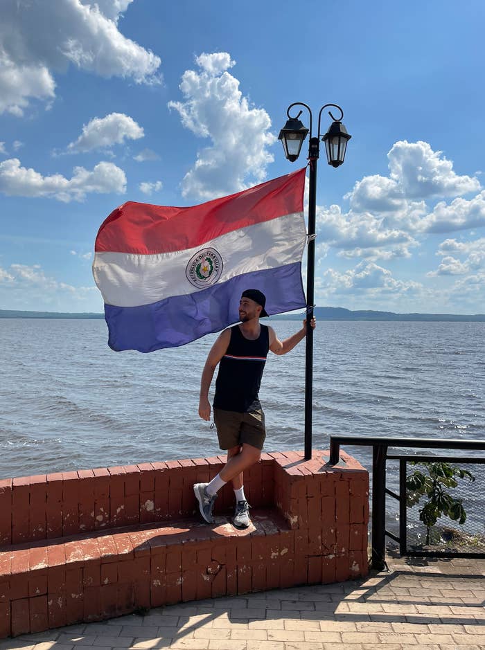 A idiosyncratic successful a sleeveless garment and shorts poses adjacent to a ample emblem by the h2o nether a partially cloudy sky