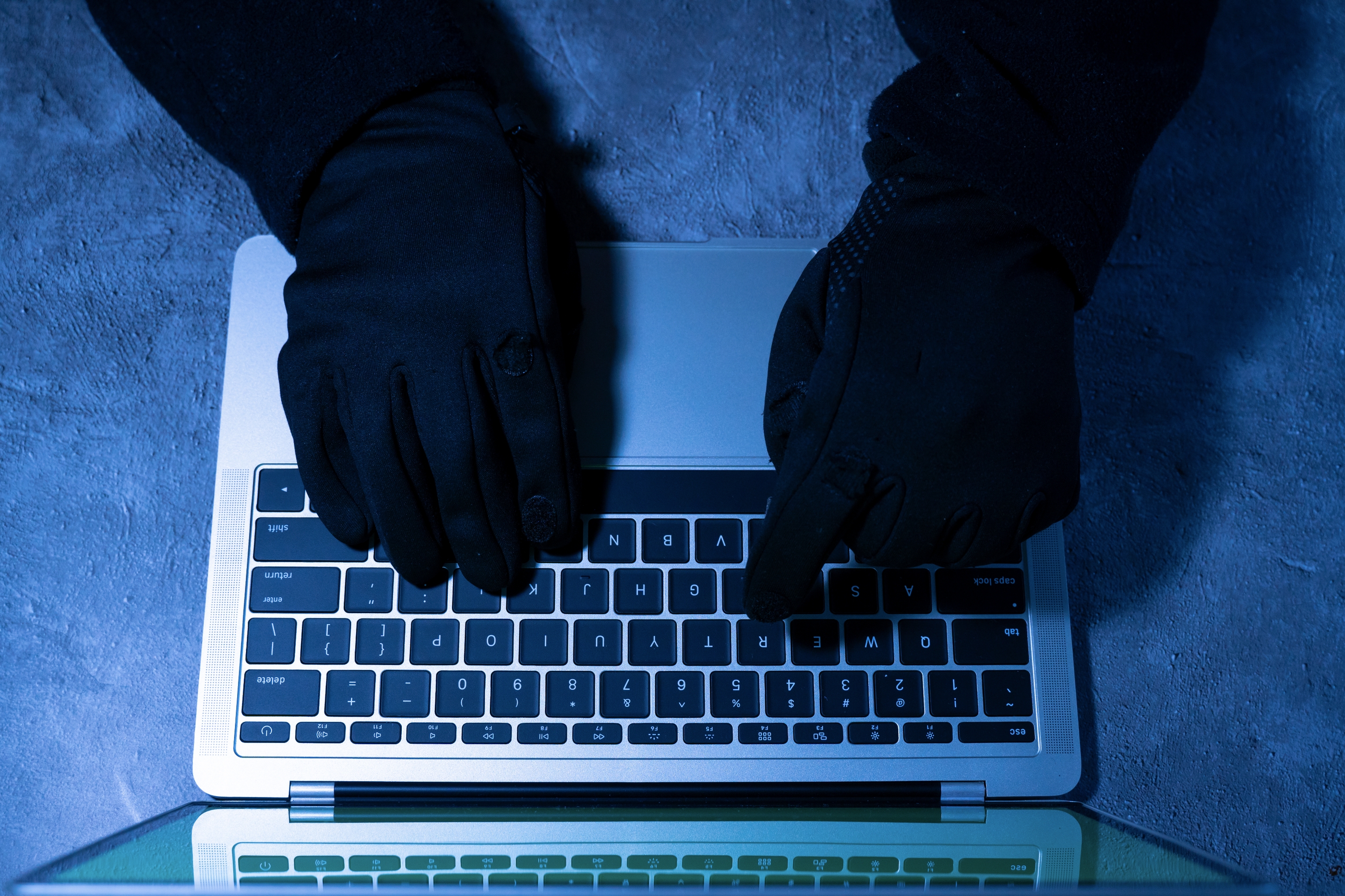 Hanskede hender som skriver på et laptop -tastatur, noe som antyder hemmelighetsfull eller sikker aktivitet