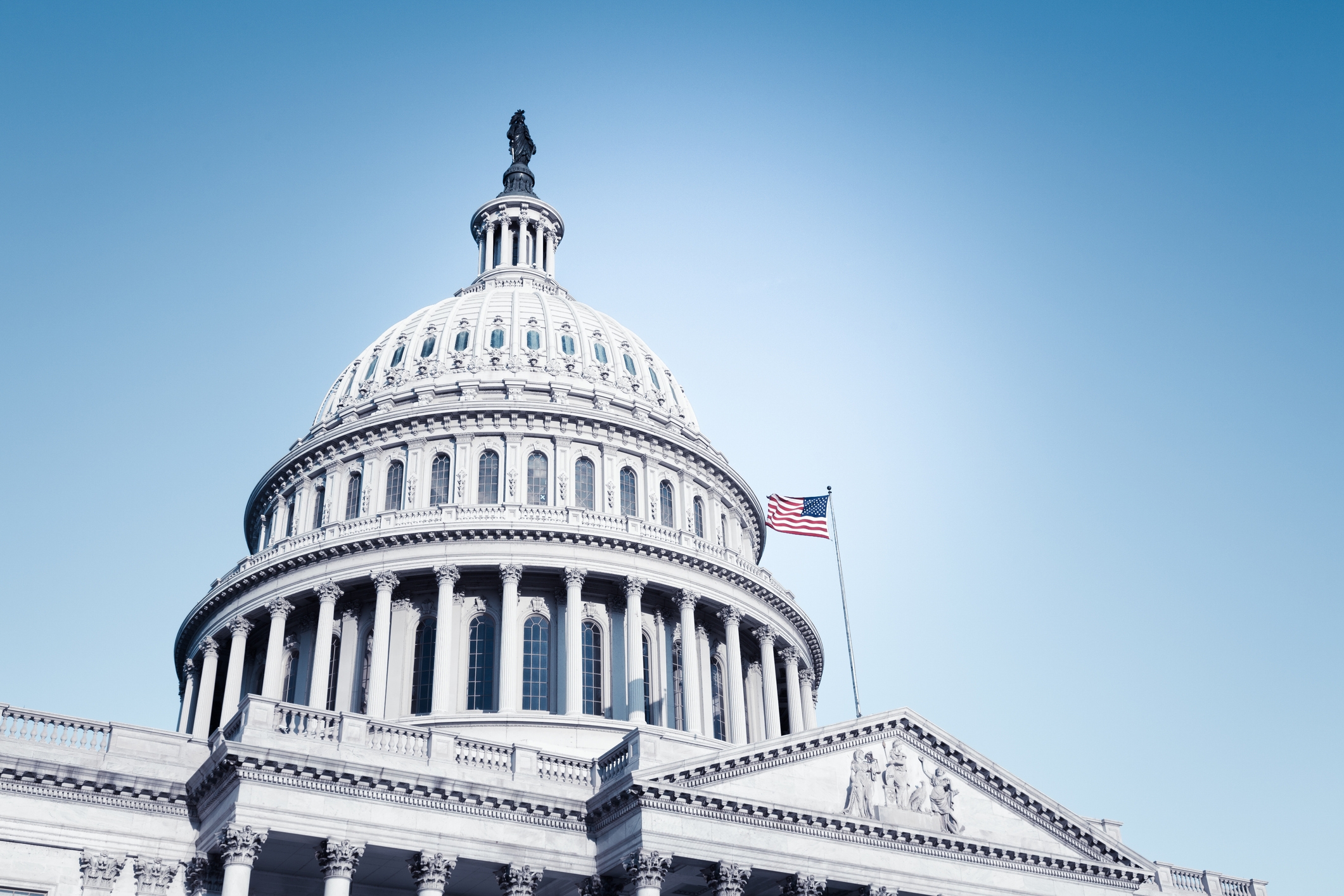 US Capitol Building under en klar himmel med et amerikansk flagg som vinker. Fremtredende kuppelstruktur som symboliserer regjering og demokrati