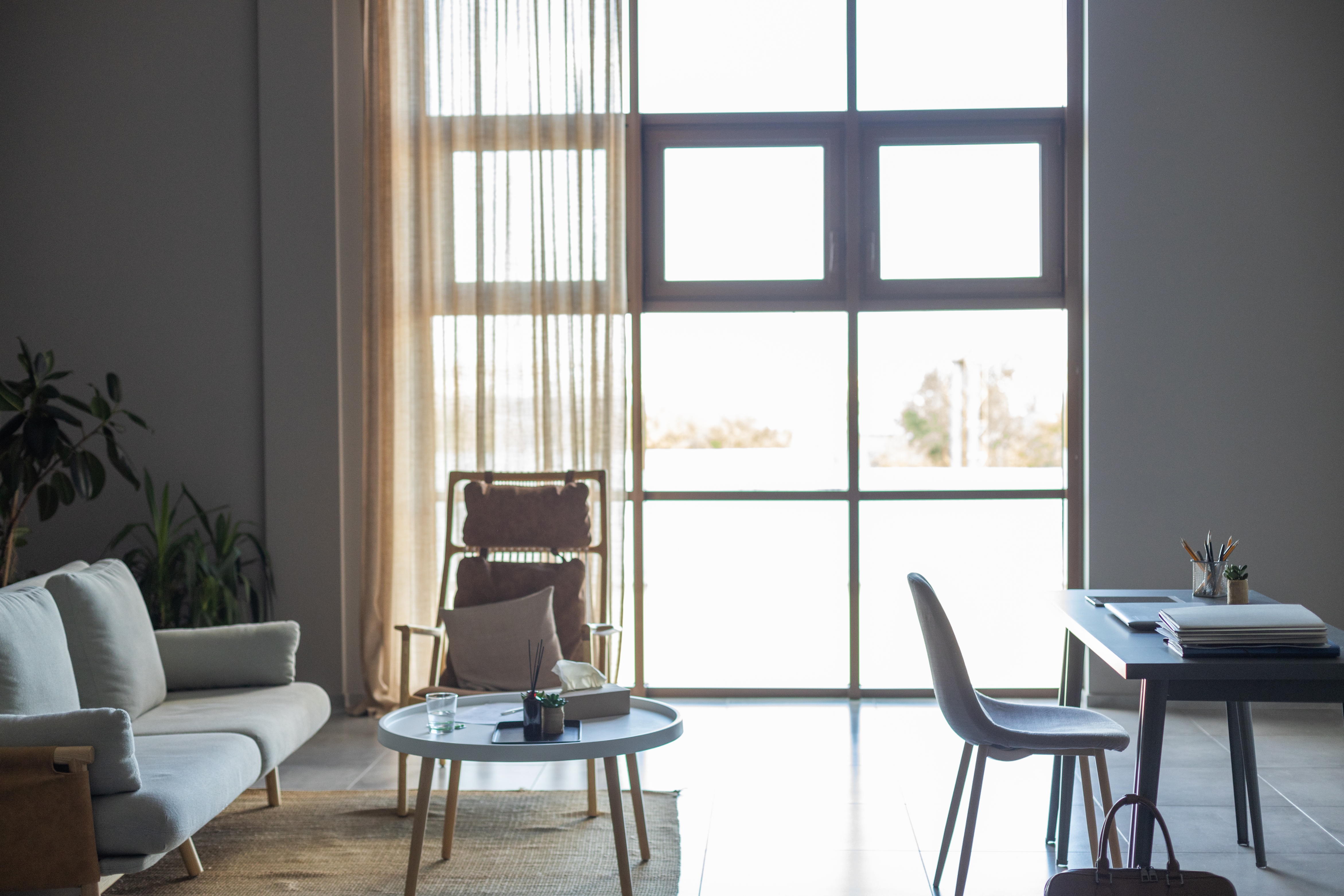 Minimalistisk stue med sofa, lenestol, salongbord og skrivebord. Stort vindu gir naturlig lys