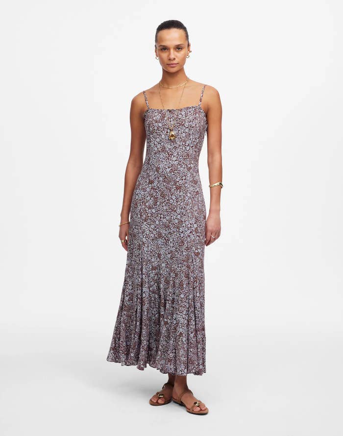 Person wearing a sleeveless, floral-patterned maxi dress, lasting  against a plain background