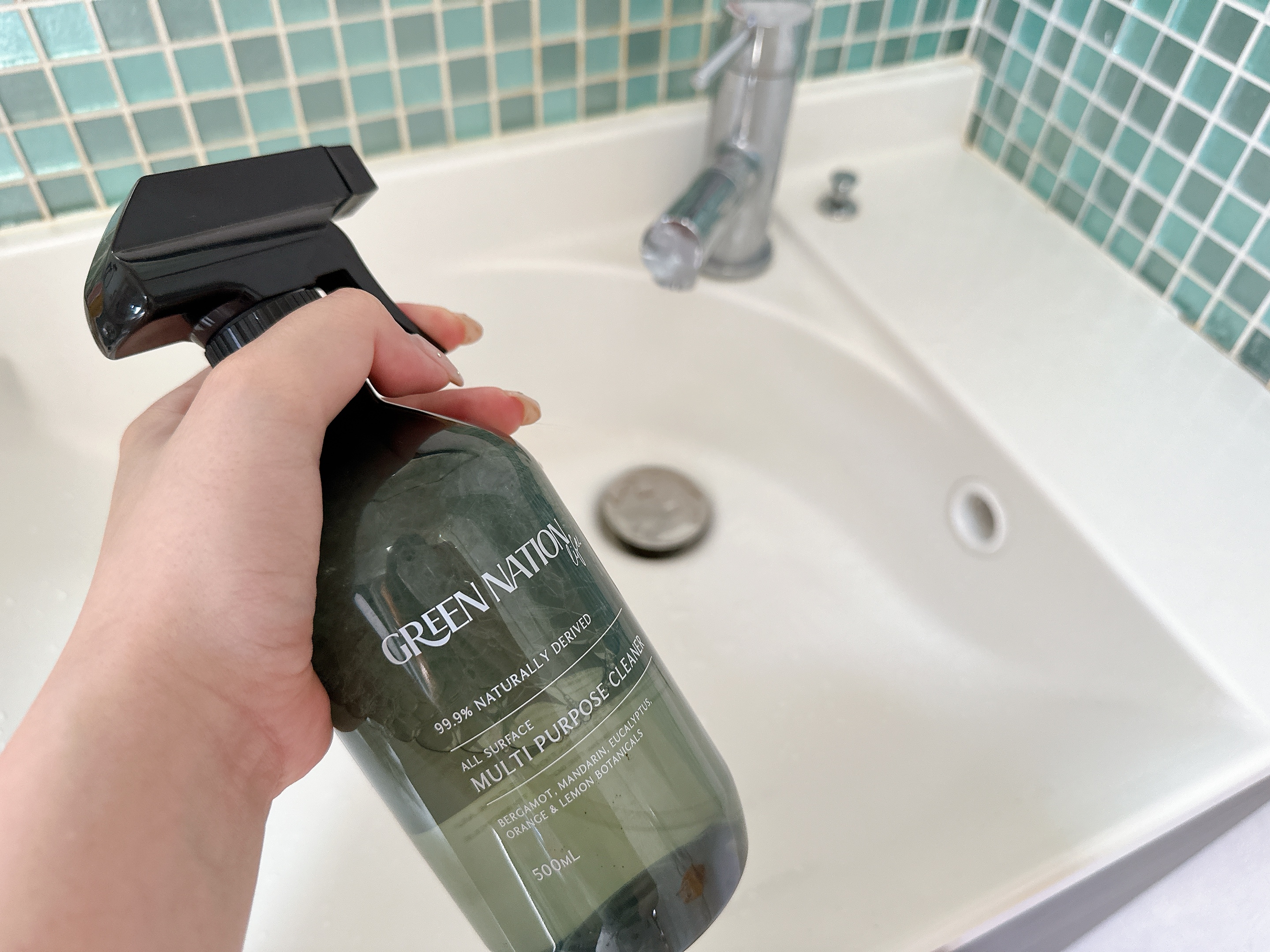 シンクの前で持たれている多目的クリーナーのスプレーボトル。タイルの背景が見える。
