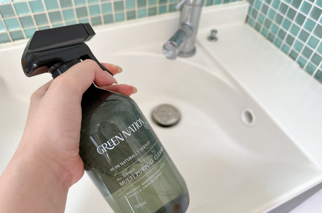 シンクの前で持たれている多目的クリーナーのスプレーボトル。タイルの背景が見える。